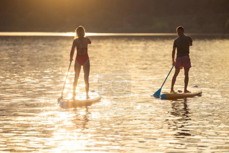 Foto de Hombre y mujer paddle sup board surfistas al atardecer. - Imagen libre de derechos