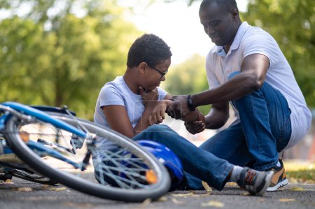 Foto de Cayendo. Papá ayudando a su hijo después de caer de una bicicleta - Imagen libre de derechos