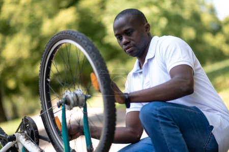 Photo for Fixing a bike. Dark-skinned man fixing a bike in the park - Royalty Free Image