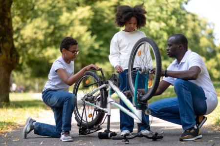 Foto de Arreglando una bicicleta. Hombre de piel oscura arreglando una bicicleta en el parque - Imagen libre de derechos