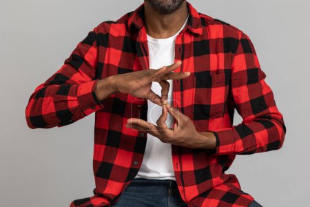 Foto de Hombre barbudo negro irreconocible con camisa a cuadros roja que muestra gestos sordomudos posando aislados sobre fondo gris del estudio. - Imagen libre de derechos