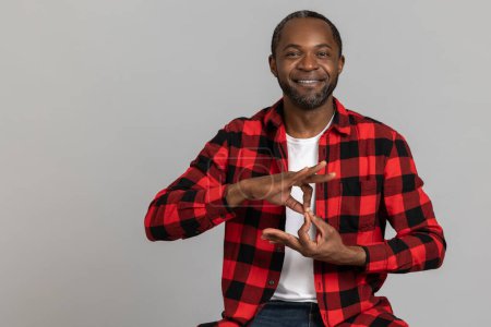 Photo for Cheerful black bearded man wearing red checkered shirt showing deaf-mute gestures posing isolated over gray studio background. - Royalty Free Image