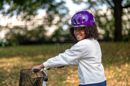 Photo for Riding a bike. Smiling dark-skinned girl on a bike in a park - Royalty Free Image