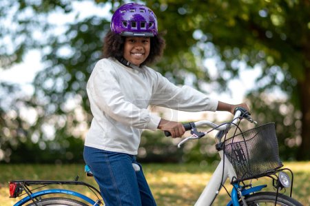 Photo for Riding a bike. Smiling dark-skinned girl on a bike in a park - Royalty Free Image