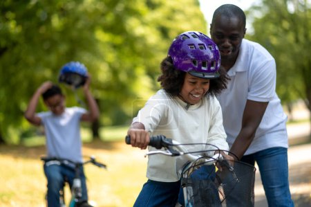 Téléchargez les photos : Roulez dans un parc. Papa heureux apprenant à ses enfants à faire du vélo - en image libre de droit