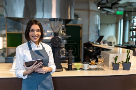 Photo for Coffee shop. Short-haired pretty girl in apron in a coffee shop - Royalty Free Image