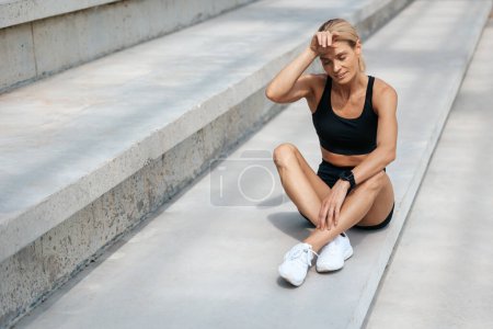 Photo for Blonde exhausted sporty woman sitting on stairs after training. - Royalty Free Image
