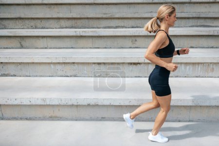 Foto de Haciendo ejercicio. Mujer rubia en ropa deportiva negro corriendo y buscando concentrado - Imagen libre de derechos