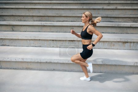 Téléchargez les photos : Faire de l'exercice. Femme blonde en tenue de sport noire courir et regarder concentré - en image libre de droit