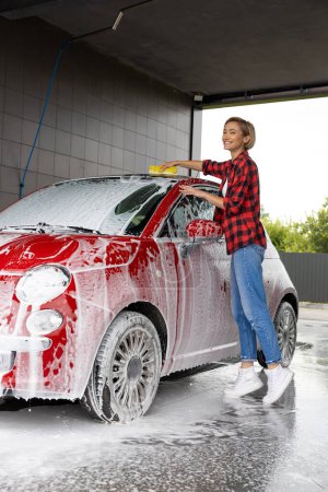 Photo for Car washing. Woman in red checkered shirt washing the car and looking busy - Royalty Free Image