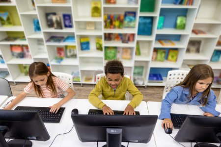 Téléchargez les photos : Groupe d'élèves qui étudient sur ordinateur dans une bibliothèque scolaire. - en image libre de droit
