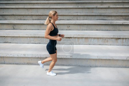 Photo for Exercising. Blonde woman in black sportswear running and looking concentrated - Royalty Free Image