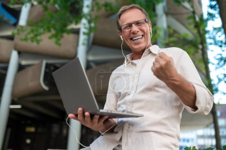 Téléchargez les photos : Homme d'âge moyen travaillant en ligne avec ordinateur portable en plein air. - en image libre de droit