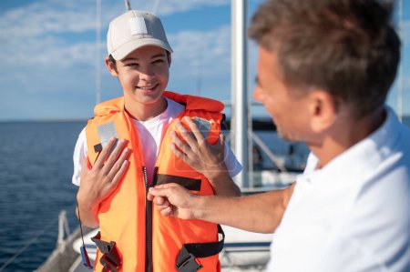 Photo for Yachting. Father putting a life-jacket on his boy while sailing on the yacht - Royalty Free Image