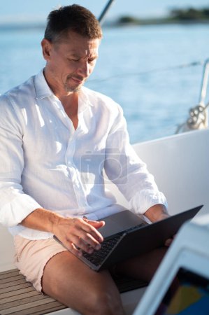 Téléchargez les photos : Numérique nomad.Successful homme mûr avec un ordinateur portable travaillant sur un yacht - en image libre de droit