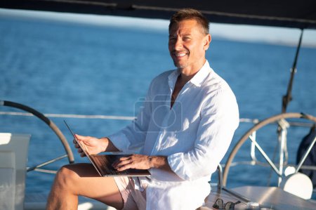 Téléchargez les photos : Numérique nomad.Successful homme mûr avec un ordinateur portable travaillant sur un yacht - en image libre de droit