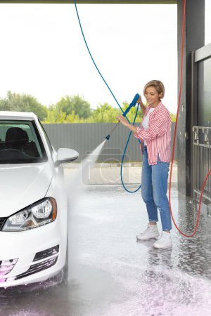 Téléchargez les photos : Jeune femme lavant la voiture au lavage de voiture et regardant impliqué - en image libre de droit