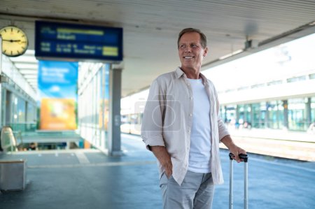 Téléchargez les photos : Heureux homme d'âge moyen avec valise debout sur le quai de la gare. - en image libre de droit