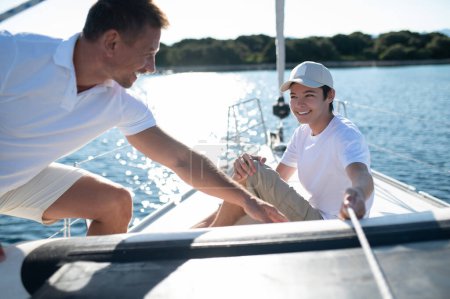 Téléchargez les photos : Journée ensoleillée sur le yacht. Père et son fils adolescent yachting par une journée ensoleillée - en image libre de droit