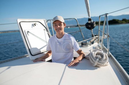 Téléchargez les photos : Garçon sur le yacht. Souriant adolescent sur un yacht à l'air satisfait - en image libre de droit