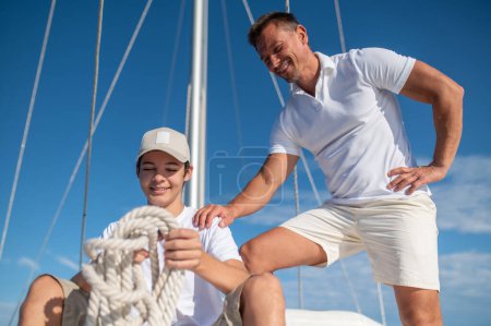 Téléchargez les photos : Journée ensoleillée. Homme mûr et son fils sur le yacht par une belle journée ensoleillée - en image libre de droit