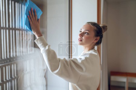Photo for Cleaning windows. Girl cleaning the window and looking concentrated - Royalty Free Image