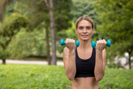 Photo for Strong athlete. Sport in the forest. Athletic woman training hands with dumbbells has workout in park. - Royalty Free Image