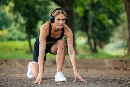 Photo for Active woman in headphones standing in lower position before starting to run. - Royalty Free Image