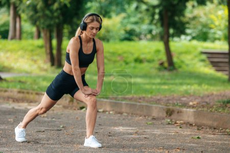 Photo for Adult sporty woman warming up before running and listening music in earphones. - Royalty Free Image