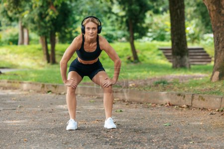 Téléchargez les photos : Femme sportive dans les écouteurs échauffement avant de faire du jogging dans le parc. - en image libre de droit