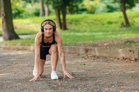 Photo for Active woman in headphones standing in lower position before starting to run. - Royalty Free Image