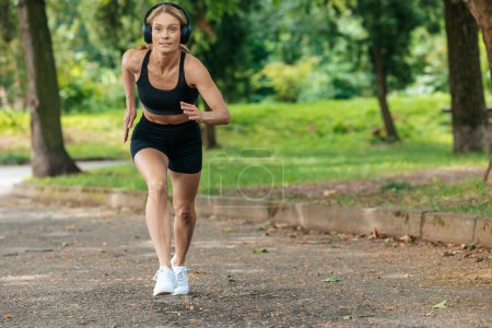 Photo for Run in nature. Healthy lifestyle. Outdoor activity. Athletic strong blonde runner woman in headphones jogging in park. - Royalty Free Image