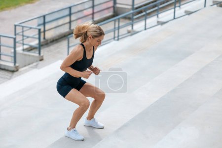 Téléchargez les photos : Faire de l'exercice. Femme blonde en vêtements de sport sautant dans les escaliers - en image libre de droit