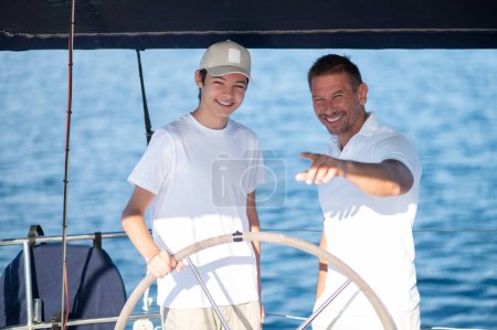 Téléchargez les photos : Au bateau. Papa montrant à son fils comment gérer le bateau - en image libre de droit