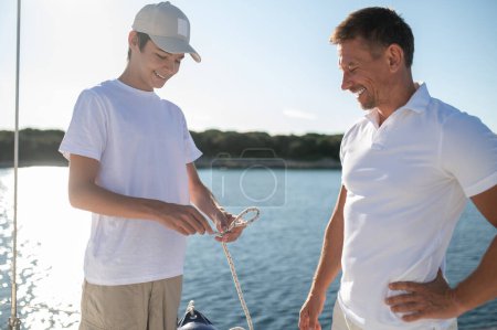Photo for Happy family. Mature man and his son spending time on the yacht and looking happy - Royalty Free Image