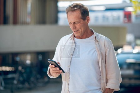 Photo for Smiling middle aged man using mobile phone in city street. - Royalty Free Image