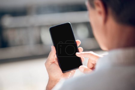 Photo for Back view of adult man looking to mobile phone with empty display with advertisement area. - Royalty Free Image