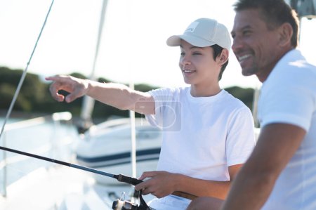 Téléchargez les photos : Avant la pêche. Adolescent et son père sur un yacht avec une canne à pêche - en image libre de droit