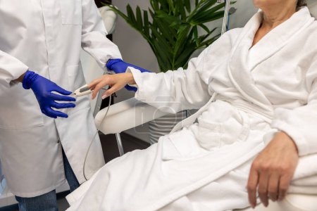 Foto de Enfermera en guantes azules comprobando el nivel de oxígeno a la paciente femenina en el salón de belleza antes de los procedimientos de cosmetología. - Imagen libre de derechos