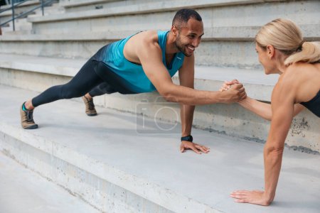 Photo for Active couple. Beautiful motivation. Multiracial sportive woman and man holding hands while standing in plank outdoor. - Royalty Free Image