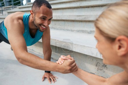 Photo for Help and effort. Together in fitness. Multiracial sportive woman and man holding hands while standing in plank outdoor. - Royalty Free Image