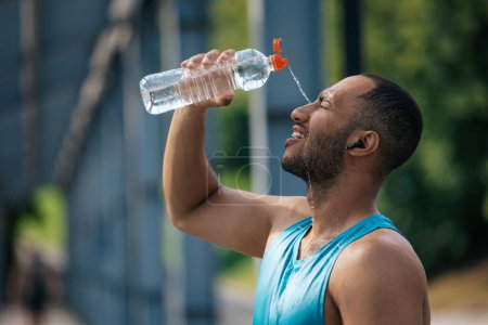 Foto de Después del entrenamiento. Joven atleta de piel oscura vertiendo un poco de agua refrescante sobre sí mismo después del entrenamiento - Imagen libre de derechos