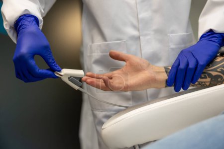 Téléchargez les photos : Infirmière mesurant la pression et le niveau d'oxygène dans le doigt masculin en clinique. - en image libre de droit