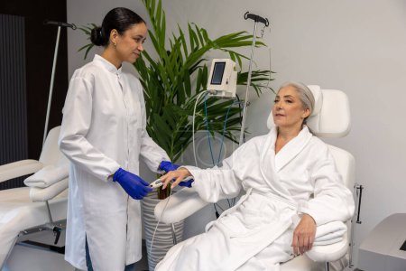 Foto de Enfermera revisando el nivel de oxígeno a través de oxímetro para paciente mayor en salón de belleza. - Imagen libre de derechos