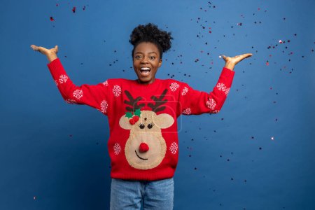 Foto de Mujer joven feliz en suéter con venado navideño extendiendo confeti - Imagen libre de derechos