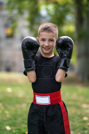 Téléchargez les photos : Petit sportif. Garçon en sportswear noir avec gants de boxe - en image libre de droit