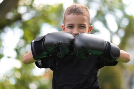 Téléchargez les photos : Kickboxer. Mignon garçon en gants de boxe à la recherche satisfait et excité - en image libre de droit
