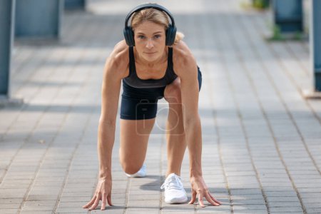 Foto de Deportiva mujer listo para correr de pie en la línea de partida pose lleva auriculares inalámbricos preparándose para maratón. - Imagen libre de derechos