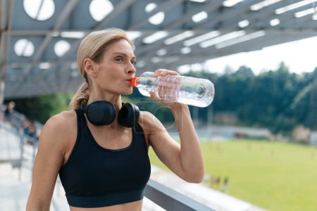 Photo for Fitness and workout wellness. Woman with headphones resting and drinking water after running. - Royalty Free Image