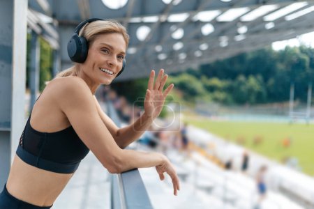 Photo for Smiling woman wearing black top and headphones greeting friend before starting workout. - Royalty Free Image